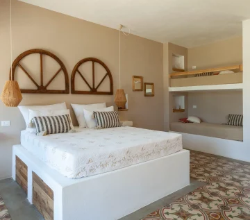 A bright, airy bedroom in the best luxury villa Salento features a double bed with white linens, patterned pillows, and wooden arch headboards. Wicker pendant lights hang above nightstands, while built-in bunk beds and colorful tiles add charm.
